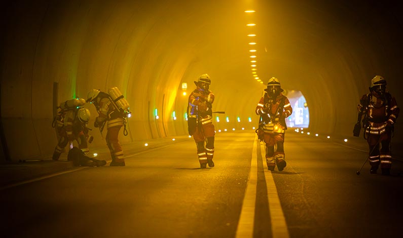 Feuerwehrleute suchen mit Stöcken den verrauchten Tunnel ab